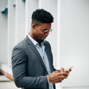 Businessman in sunglasses smiling down at phone while using business texting